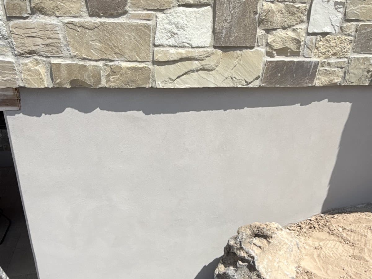 Smooth gray foundation parge coat below natural stone veneer