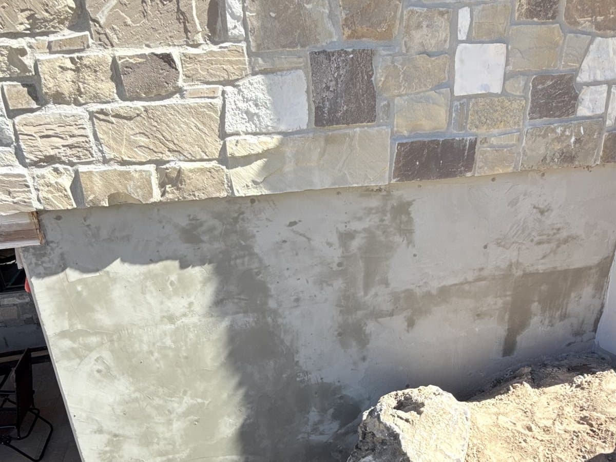Stone veneer meeting a freshly plastered foundation base