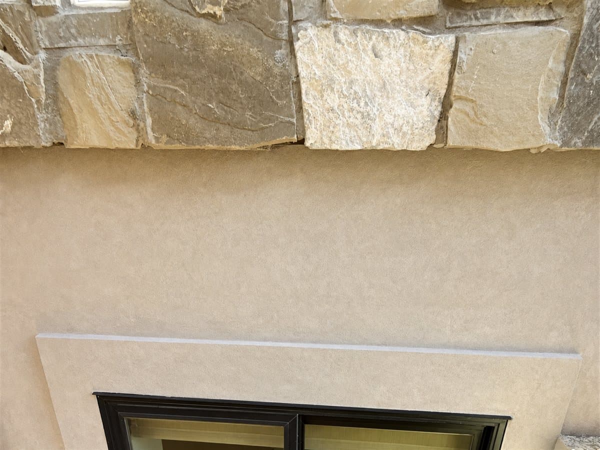 Natural stone veneer above a cream stucco wall and black-framed window