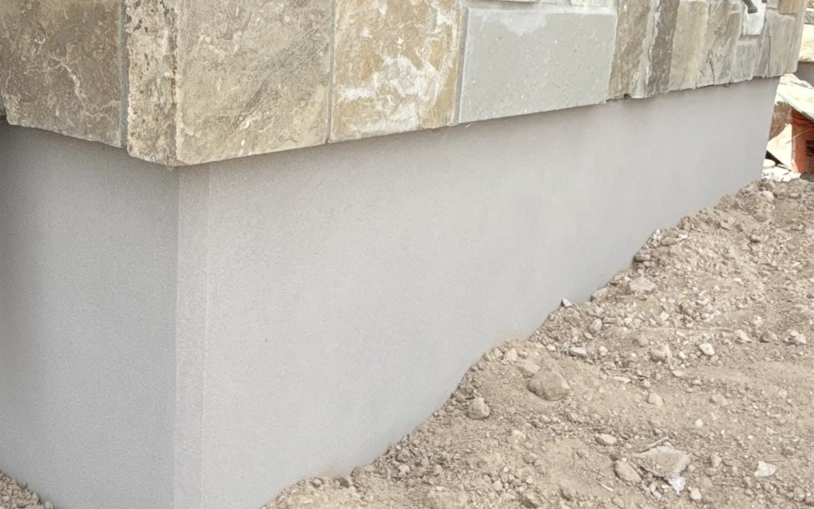 Smooth gray parge coat meeting natural stone veneer at a home's foundation