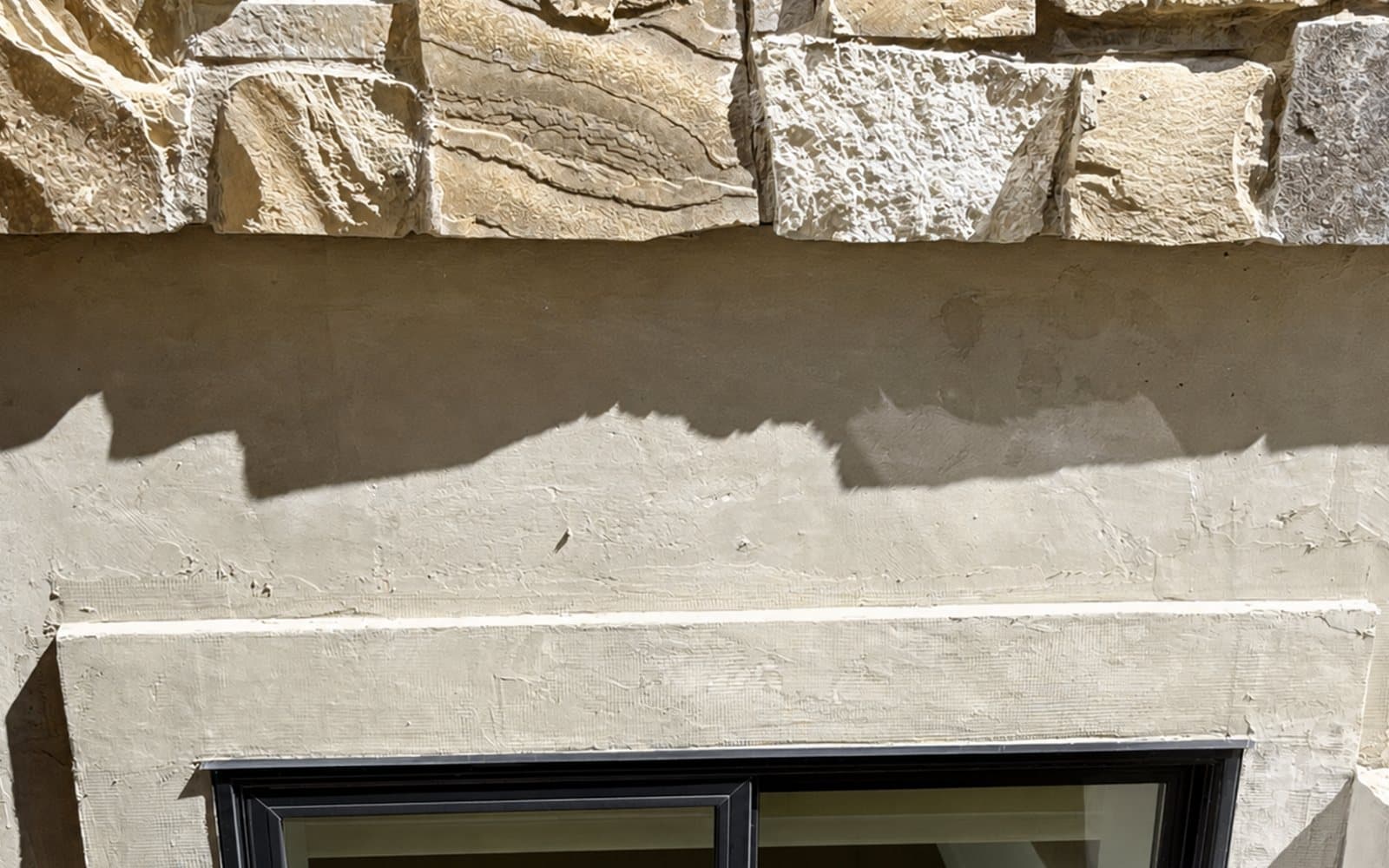 Natural stone veneer meeting cream stucco above a black-framed window